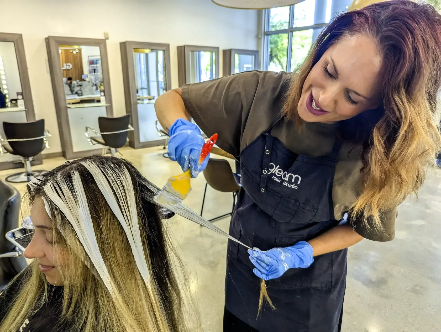 Stylist applying hair color to a client’s sectioned hair at Gleam Hair Studio